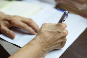 Selective focus at elderly hand using blue pen to writing letter about nursing home abuse.