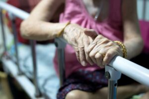 Hand of elderly woman holding a bed rail, highlighting vulnerability and the importance of safety in nursing homes.