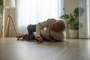 An elderly Asian man falls to the ground while using a walker at home. The senior grandfather experiences an accident after attempting physical therapy alone.