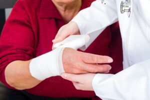 Photo of a doctor bandaging an elderly woman's thumb. 