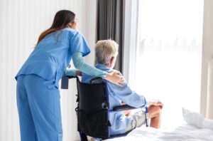 A caregiver nurse takes care of a senior patient sitting in a wheelchair. The nurse assists the elderly man.