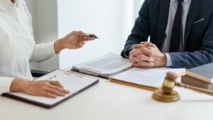 A man in a dark blue suit, a lawyer, sitting at his desk, preparing to provide legal consultation to his client with the help of his assistant.