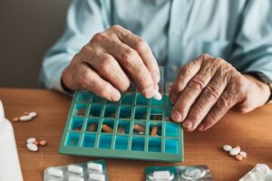 Elderly man sorting his medications into a pill organizer. Healthcare and senior wellness concept.