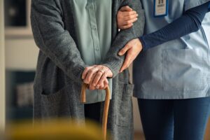 Close-up of a caregiver doctor helping an elderly woman at a clinic. The nurse holds a senior patient using a walking stick.