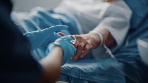 A senior female patient rests in a bed, with a pulse oximeter on her finger showing her heart rate. 