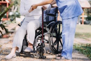 A young Asian physical therapist assisting an elderly woman with walking using a walker. 2/2 