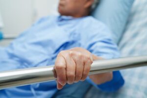 Asian elderly woman patient holding a bed rail while lying down, waiting hopefully for her family in the hospital.