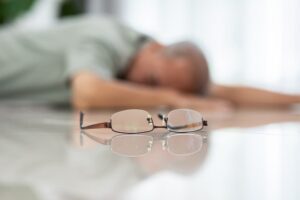 A senior Asian man falls from a chair, losing consciousness while alone at home.