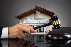 Close-up of a judge hitting a gavel next to a house model on a grey background.