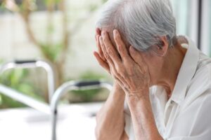 A depressed Asian senior woman with anxiety and a depressive illness sits alone at home, crying and visibly tired. She struggles with the debilitating effects of her condition.